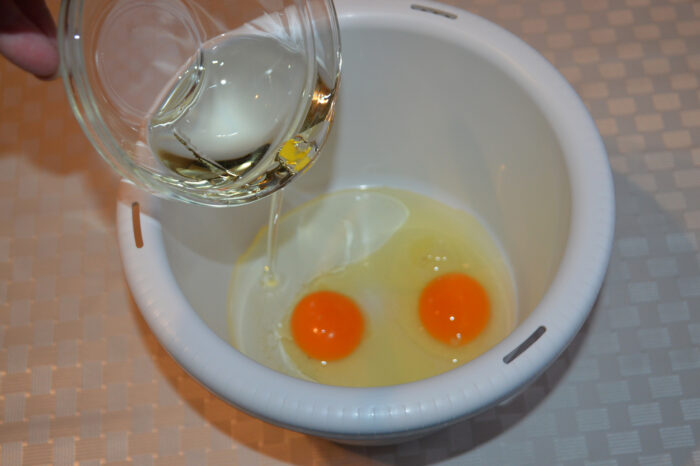 Pouring neutral oil over beaten eggs in a bowl