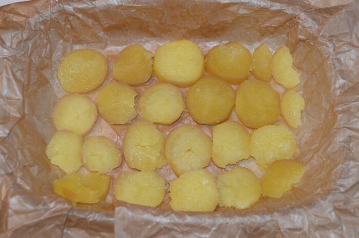 Baking dish lined with parchment and a first layer of sliced boiled potatoes