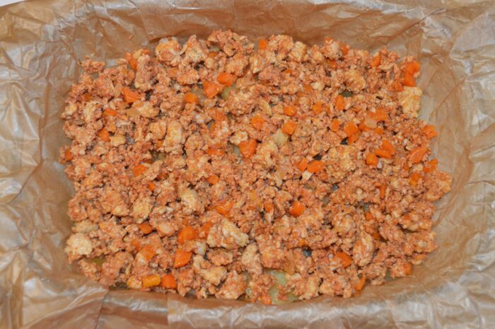 First layer of ground chicken filling spread over the potatoes in the baking dish