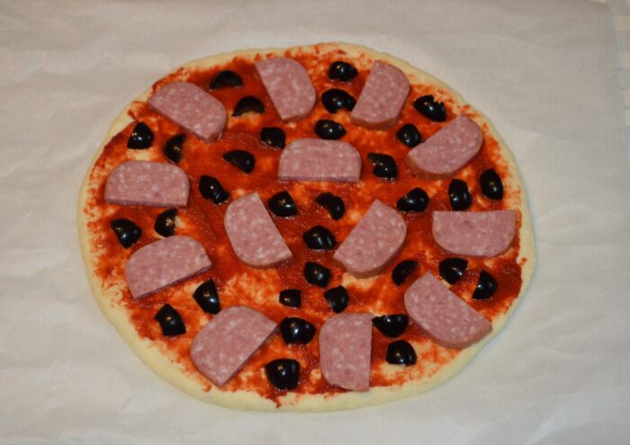 Chopped black olives sprinkled over the salami on the pizza