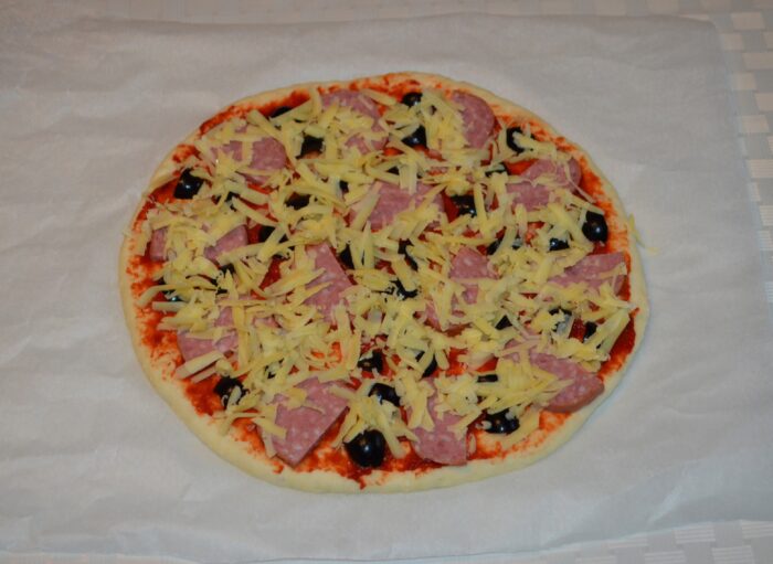 Pizza topped with grated cheese going into the hot oven