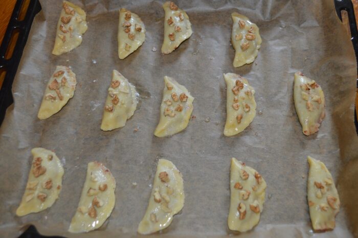 Crescents topped with chopped walnuts baking in the oven until lightly golden