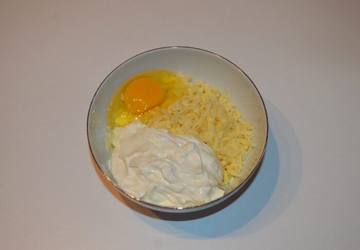 Grated cheese, sour cream and egg in a bowl being mixed into a smooth sauce