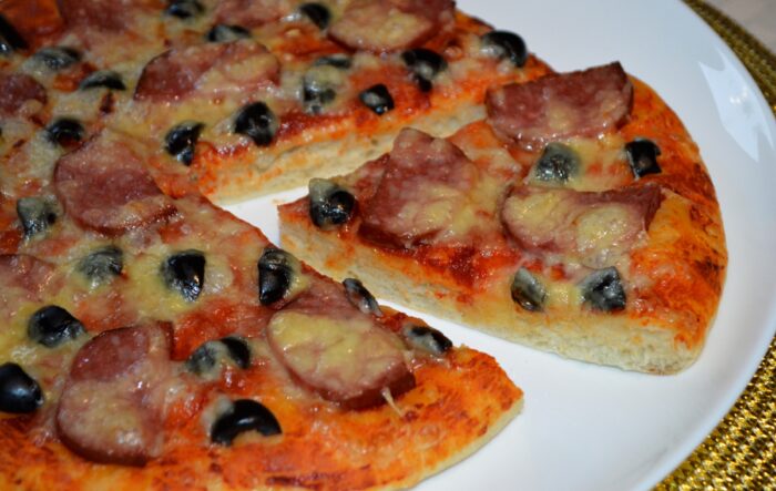 Baked pizza with salami, cheese and olives sliced and ready to serve