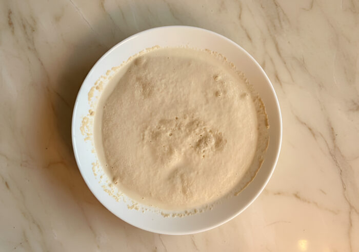 Yeast mixture in a glass bowl with milk and sugar, starting to foam