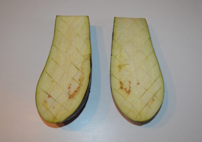 Eggplant halves with the flesh scored in a crosshatch diamond pattern