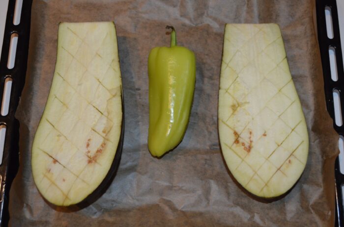 Eggplant halves and a whole red bell pepper arranged on a parchment-lined baking tray
