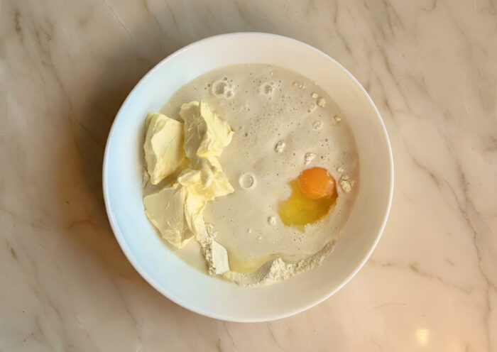 Milk and yeast mixture, egg, and soft butter added over flour in a bowl