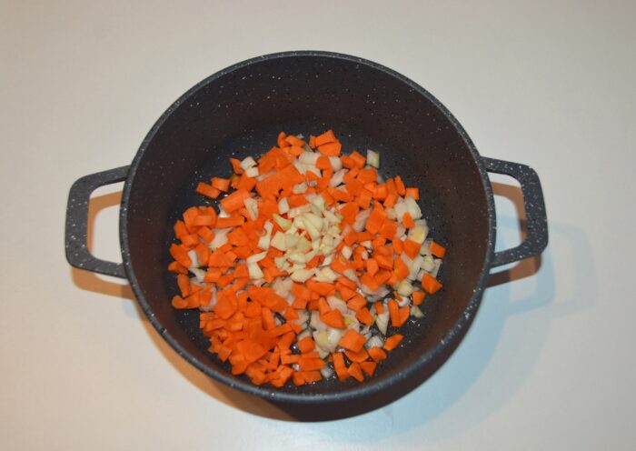Minced garlic being added on top of sautéed onion and carrot