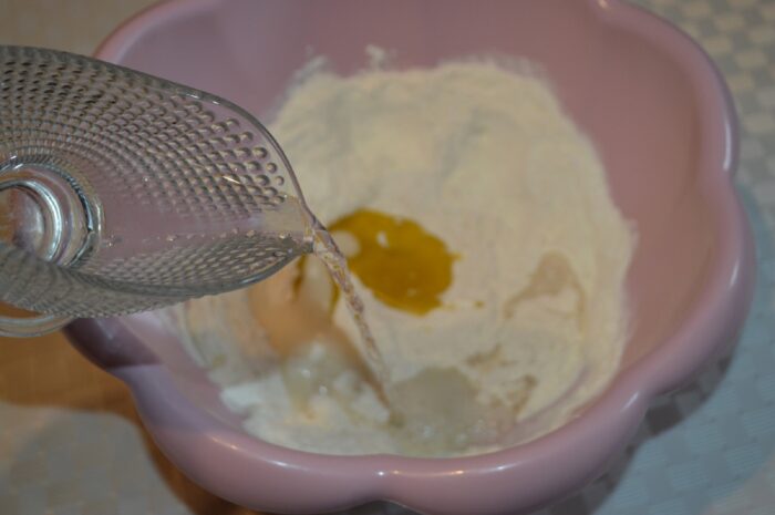Warm water being added to the bowl to form pizza dough