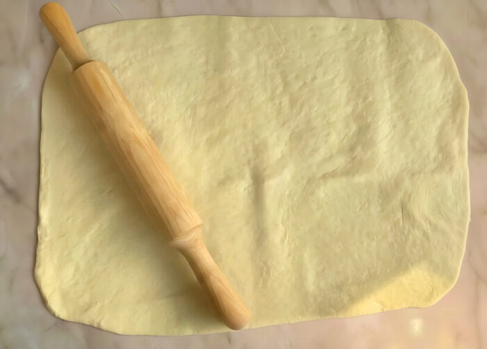 Rolled-out dough into a rectangle, with a bowl of cinnamon sugar nearby