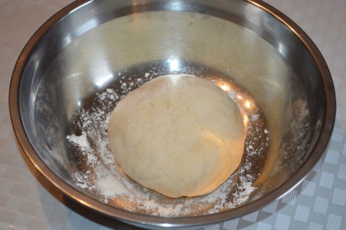 Kneaded pizza dough resting in a floured bowl to rise