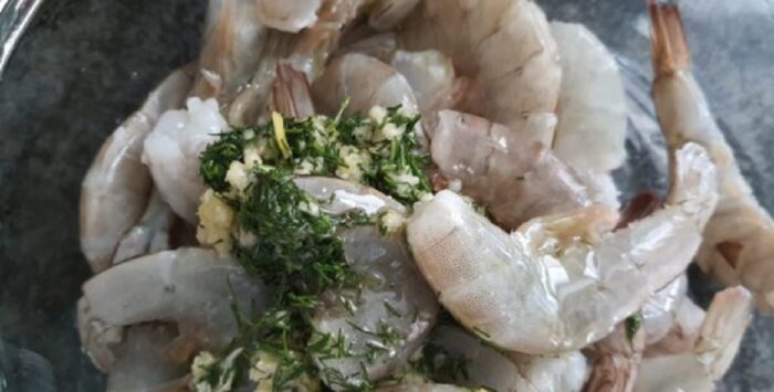 Raw shrimp in a bowl topped with garlic, dill, olive oil, and salt