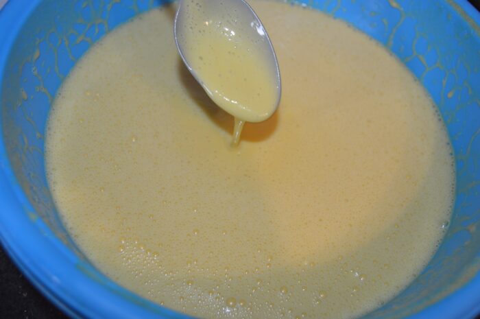 Close‑up of the thin, glossy batter running off a ladle into the bowl