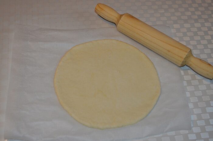 Pizza dough rolled into a round on parchment paper