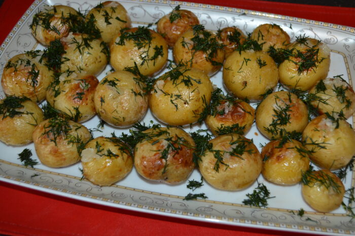 Roasted new potatoes on a plate topped with garlic sauce and fresh dill