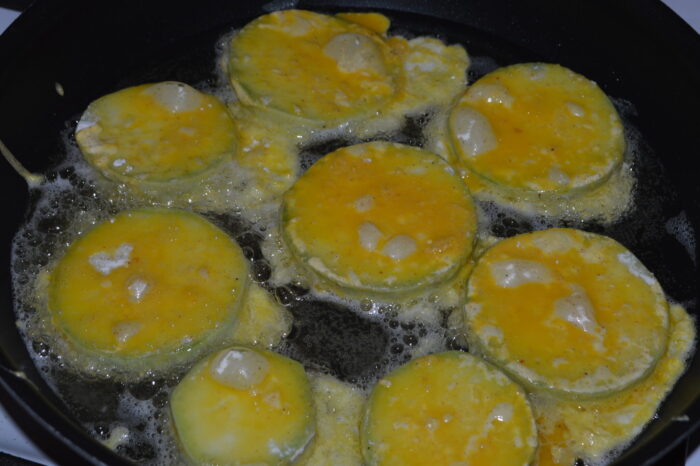 Rodajas de calabacín empanadas friéndose en una sartén con aceite